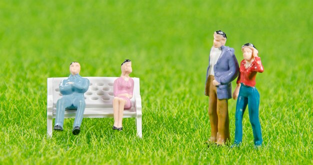 Mini toy man and woman sitting on a chair with other couple on a grass field