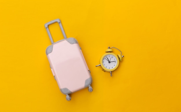 Mini Travel luggage and alarm clock on yellow background. 