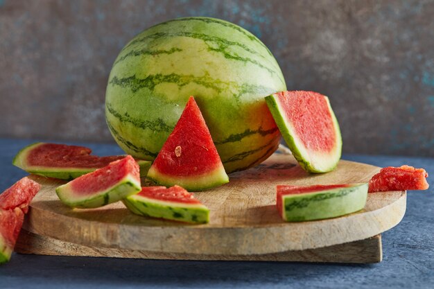 Mini Watermeloen met in plakjes gesneden partjes op een ronde houten standaard op een blauw.