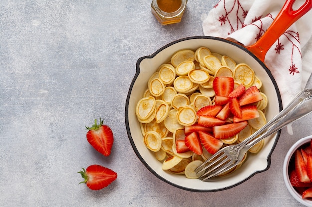 Mini white pancake cereal with strawberries in frying pan for breakfast on grey background