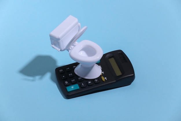 Mini white toilet and calculator on blue background with deep shadow. Minimalism.