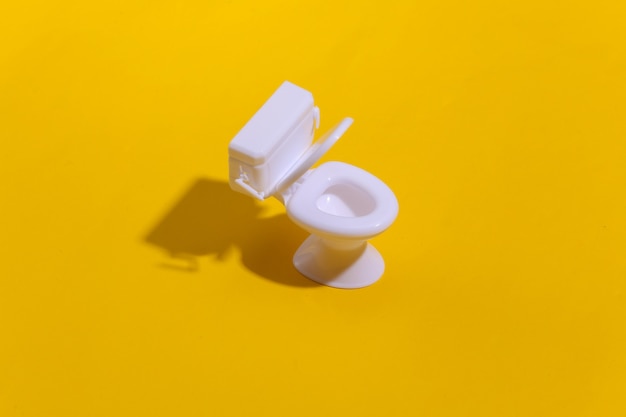 Mini white toilet on yellow background with deep shadow. Minimalism.