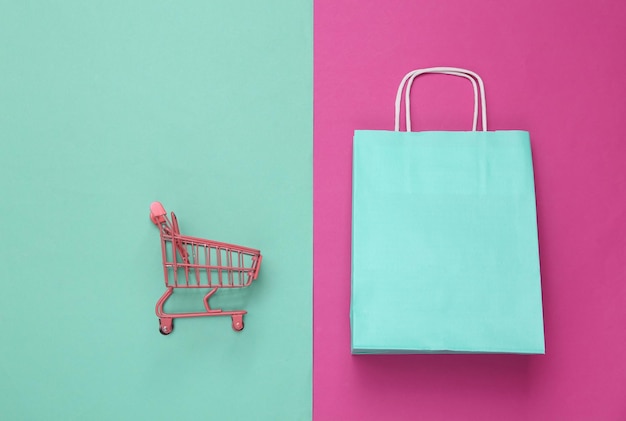 Mini winkelwagentje en papieren boodschappenpakket op roze blauwe achtergrond Bovenaanzicht Minimalisme