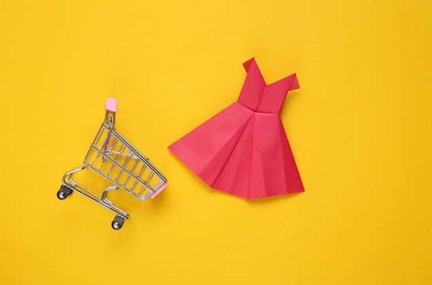 Mini winkelwagentje met Origami papier rode jurk op gele achtergrond Shopping concept