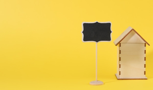 Мини-деревянный дом и указатель мела на желтой поверхности. Концепция покупки недвижимости, ипотека и ремонт дома