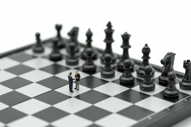 Миниатюрные 2 человека бизнесмены пожимают друг другу руки на шахматной доске с шахматной фигурой