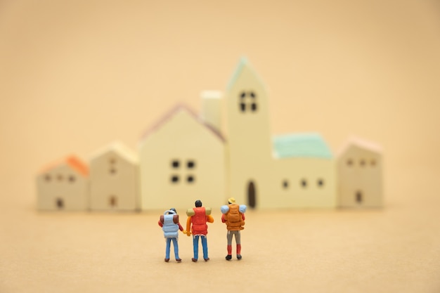 Миниатюрные 3 человека стоят на моделях домов и отелей, чтобы выбрать место для проживания.