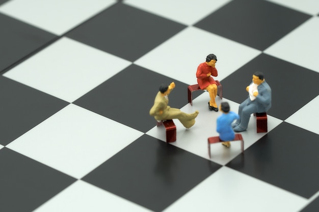 Miniature 4 people sitting on red staples placed on a a chessboard. 