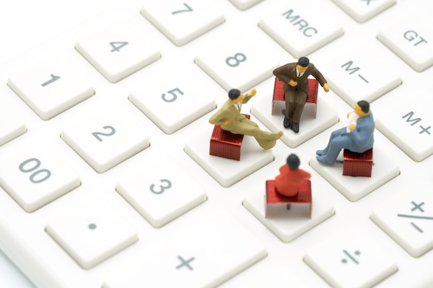 Miniature 4 people sitting on red staples placed on a white calculator. 