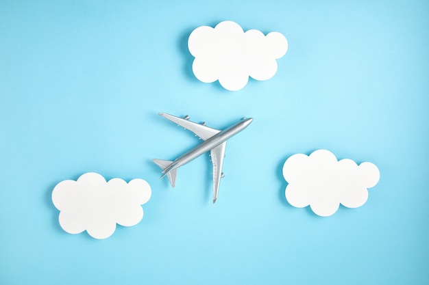 종이 구름과 파란색 벽에 미니어처 비행기입니다. 여행 관광, 항공사, 저가 항공편 개념. 평면도, 평면 누워.