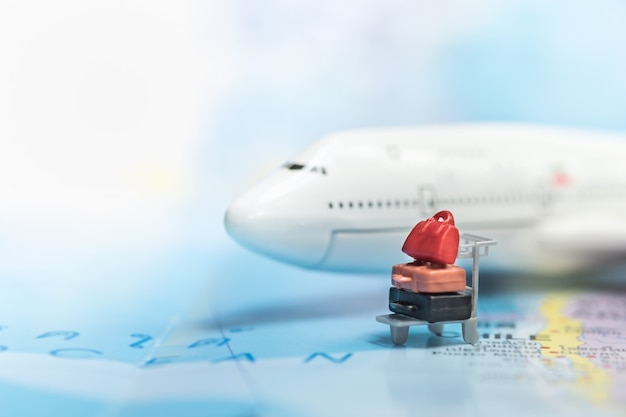 Фото Миниатюрная багажная тележка для аэропорта с чемоданами на карте мира и рядом с мини-моделью самолета.