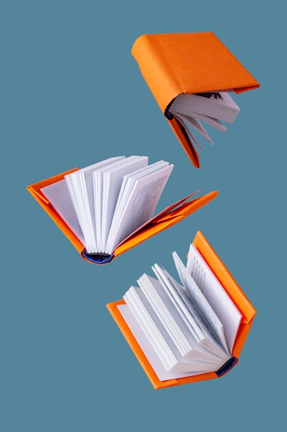 Photo miniature books in an orange cover fly on a blue background