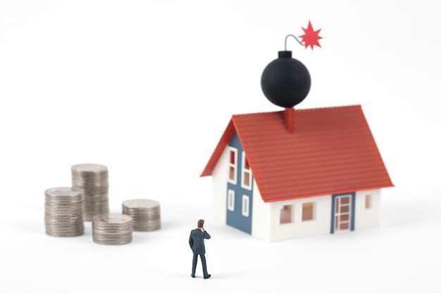 Miniature business man and coins with bomb on the model house roof