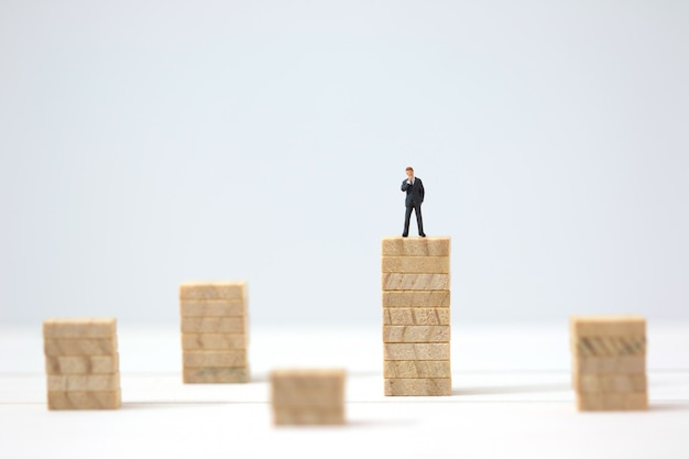 Miniature businessman making the decision on highest wooden stacks.