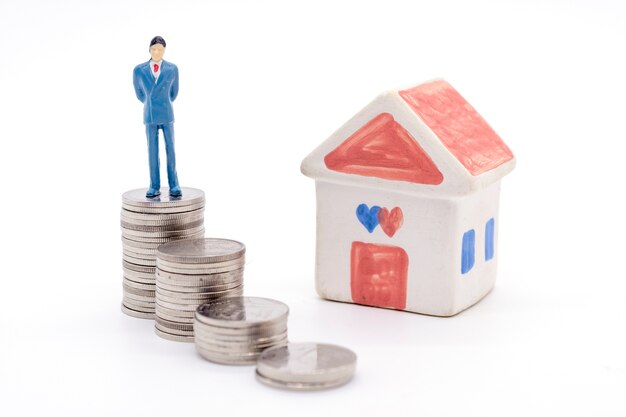 Miniature businessman standing on coins and the house behind. saving and loan concept. 