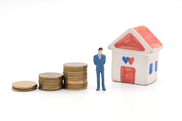 Miniature businessman standing on coins and the house behind. saving and loan concept. 