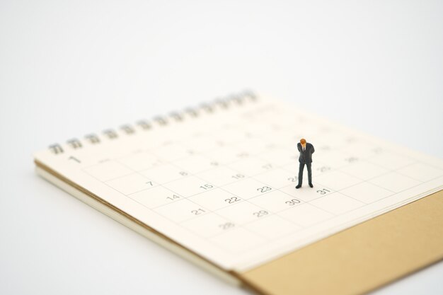 Uomo d'affari miniatura che sta sul calendario bianco