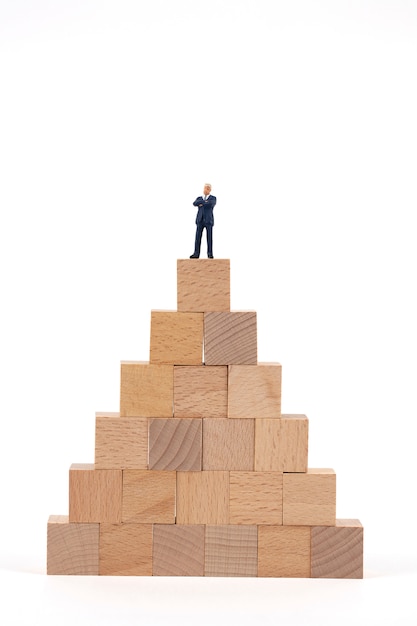 木製のブロックの上に立ってミニチュア実業家