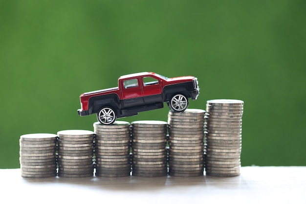 Miniature car model on growing stack of coins money on nature\
green background, saving money for car, finance and car loan,\
investment and business concept