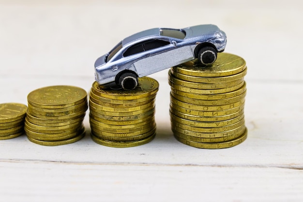 Miniature car model on stacks of golden coins on white wooden background