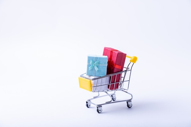 Miniature cart with gifts on a white surface. Holidays shopping concept. Close-up.