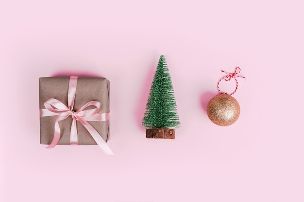 Foto albero di natale in miniatura, regalo avvolto in carta del mestiere e decorazione della palla dell'albero di natale sul rosa pallido.