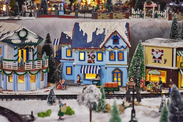 Miniature colored houses and figures of people during celebration of Christmas, snowy streets, and glowing lanterns. Miniature toy city during winter season. City scene in miniature models