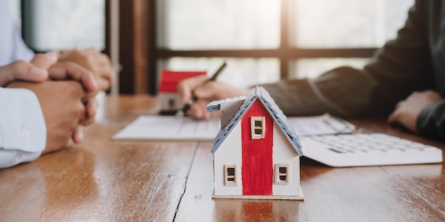 Miniature of cottage house on table close up view happy African family agency or bank clients handshake real estate agent after contract signing on blurred background