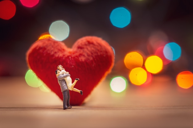 miniature couple standing on red heart