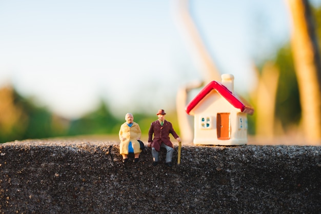 Miniature elderly people sitting with mini house