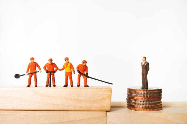 Miniature engineers and businessman standing on stack coins 