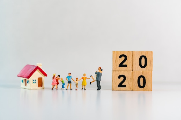 Famiglia in miniatura in piedi con mini casa e blocchi di legno 2020