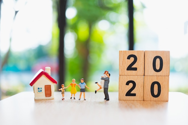 Famiglia in miniatura in piedi con mini casa e blocchi di legno 2020