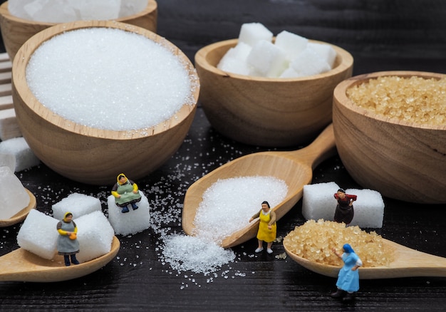 Miniature fat woman near wooden bowl with sugar cube on dark wood background.