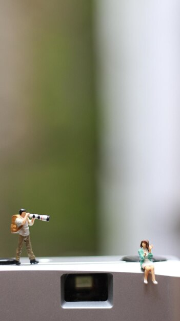 Photo a miniature figure taking picture with a camera against a real camera in the background