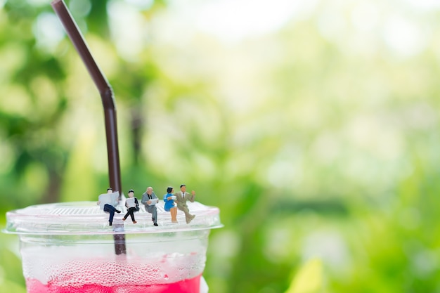 Photo miniature figures are reading a book and sitting on the plastic cup of drink