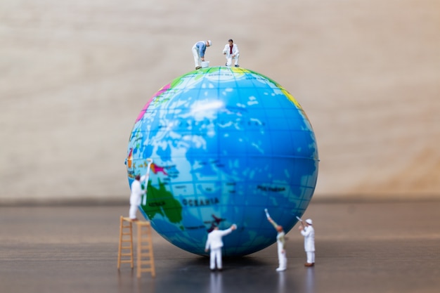 miniature figures of painters are painting  the globe 
