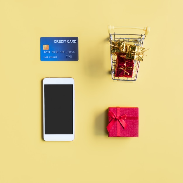 Miniature of gift boxes in trolley, credit card and smartphone on yellow background