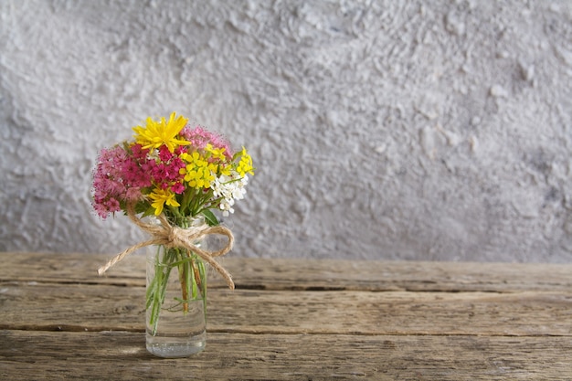 Miniature glass bottle with flowers on wooden table and concrete wall with sunlight with copy space