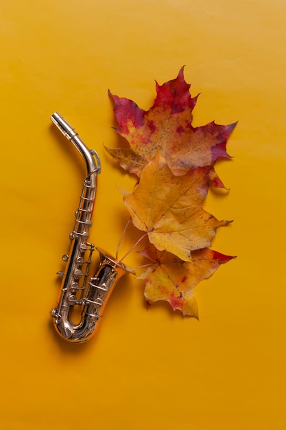 Foto copia in miniatura del sassofono dorato sulle foglie gialle dell'acero d'autunno sullo sfondo vista superiore da vicino