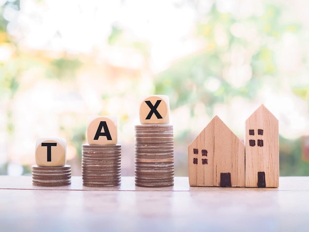 Casa in miniatura e blocchi di legno con la parola tassa sulla pila di monete il concetto di pagamento delle tasse per la casa e la proprietà tasse di proprietà