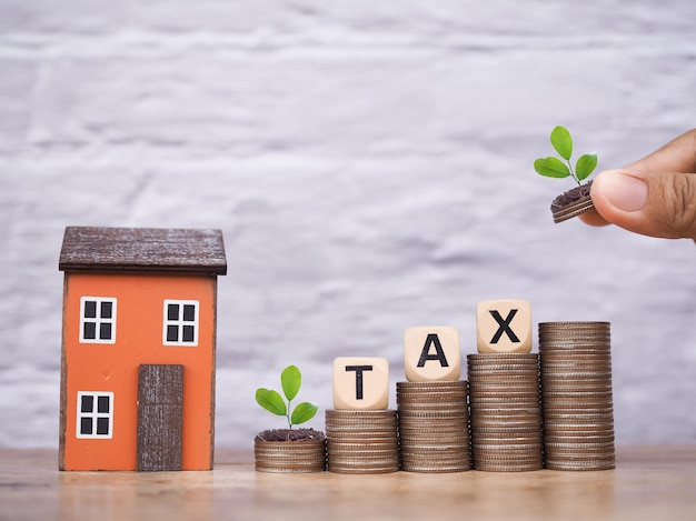 미니어처 집과 동전 어리에 TAX라는 단어가 새겨진 나무 블록 집에 대한 지불 세금 개념 부동산 투자 집 모기지 부동산