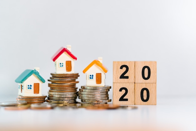 Miniature houses on stack of coins with year 2020 in wooden blocks