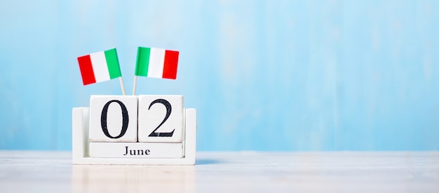 Bandiera dell'italia in miniatura con calendario di giugno su tavolo bianco e sfondo blu della parete