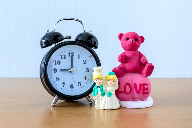 Miniature married couple and teddy bear and clock on wooden. concept for wedding & valentine Day.