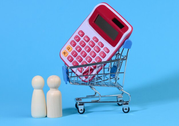 Miniature metal shopping cart with calculator and wooden family. concept of budget control, close up