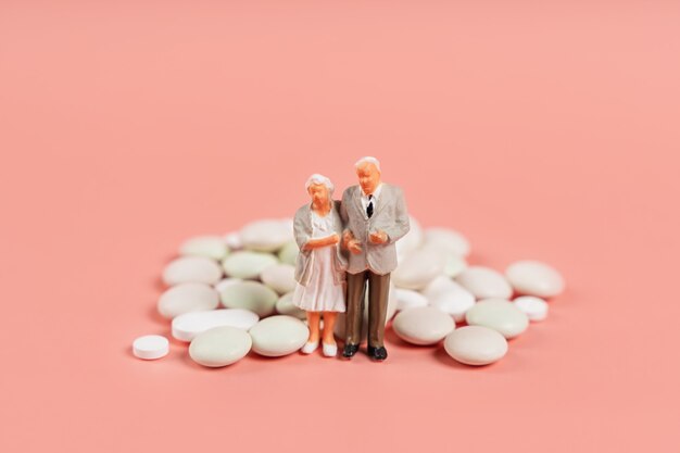 Miniature models of elderly people stand near a handful of pills Painful old age