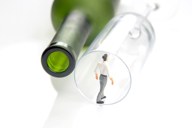 Miniature people alcohol addiction problem concept an alcoholic stands on the edge of a glass near a wine bottle