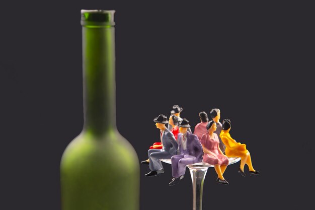 Miniature people. alcohol addiction problem concept. people sit on the edge of a wine glass near the bottle