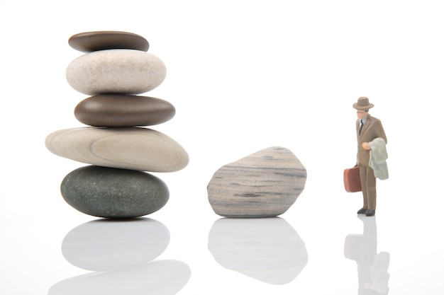 Miniature people a business man stands near a stone pyramid on a white background life balance